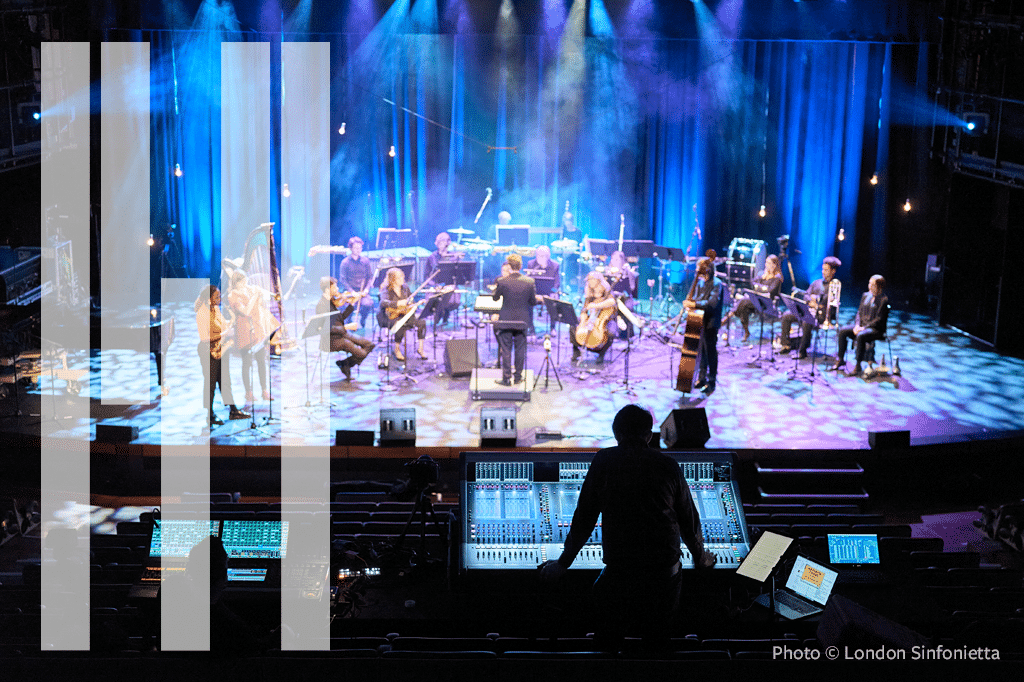 London Sinfonietta kuvattuna sinivioletissa valossa. Kuvan etualalla on äänitarkkailija pöytänsä ääressä.